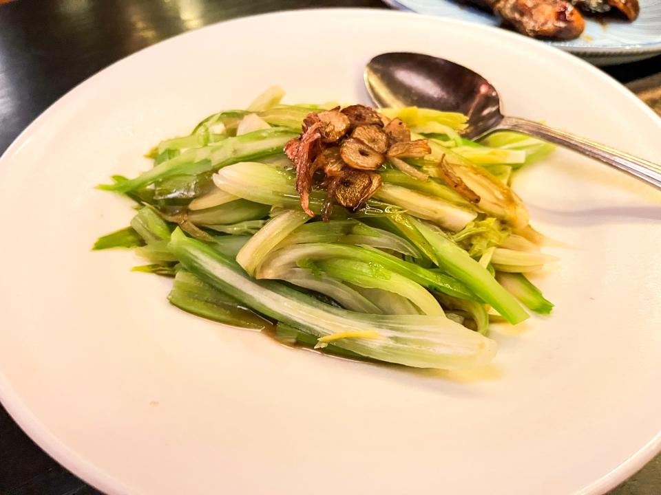 A white plate filled with pieces of celery with garlic pieces on top and a metal spoon on the plate.