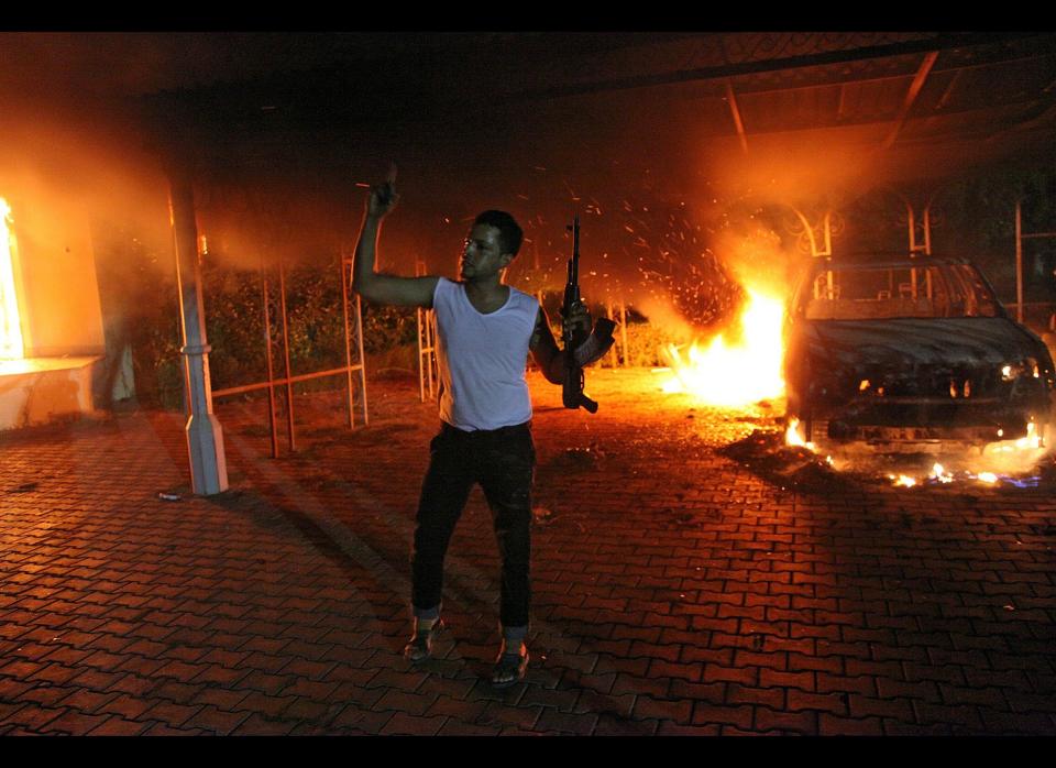 An armed man waves his rifle as buildings and cars are engulfed in flames after being set on fire inside the US consulate compound in Benghazi, late on September 11, 2012. (STR/AFP/GettyImages)