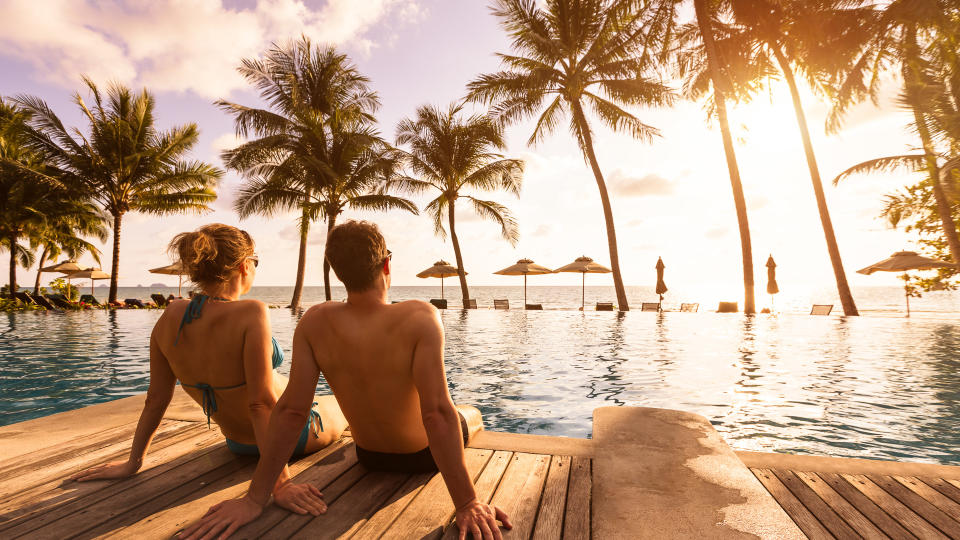 Couple enjoying beach vacation holidays at tropical resort with swimming pool and coconut palm trees near the coast with beautiful landscape at sunset, honeymoon destination.