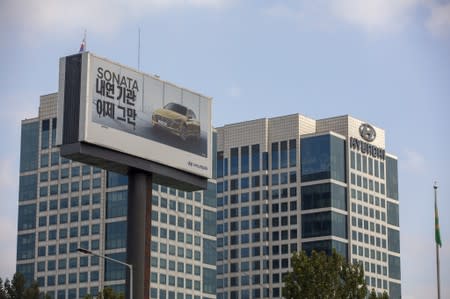 A man writes a message on an advertisement promoting Hyundai Motor's sedan Sonata in front of Hyundai Motor's headquarter building in Seoul