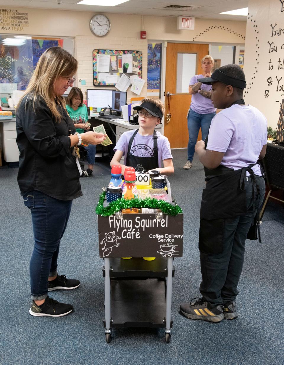 Rhodes Elementary students and Flying Squirrel Cafe employees Max Mullican and JD Bryant deliver coffee to the school's principal, Kacie Reaves, on Friday, Dec. 1, 2023. The student-run business helps teach the children life and social skills.