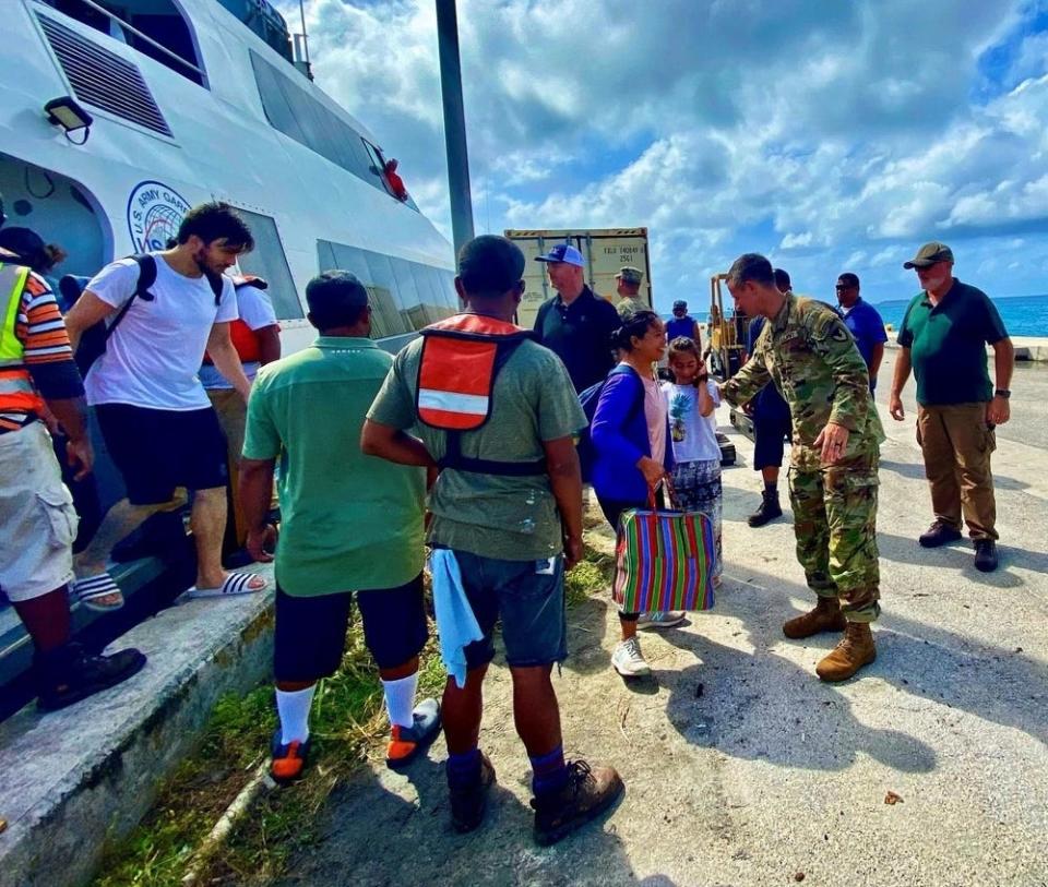 people exiting a boat are greeted by an army commander in uniform