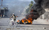 Un ciclista pasa cerca de neumáticos encendidos por manifestantes que exigen saber cómo las administraciones actuales y pasadas de Haití utilizaron los fondos de un acuerdo petrolero con Venezuela en Puerto Príncipe, el miércoles 17 de octubre de 2018. (AP Foto / Dieu Nalio Chery)