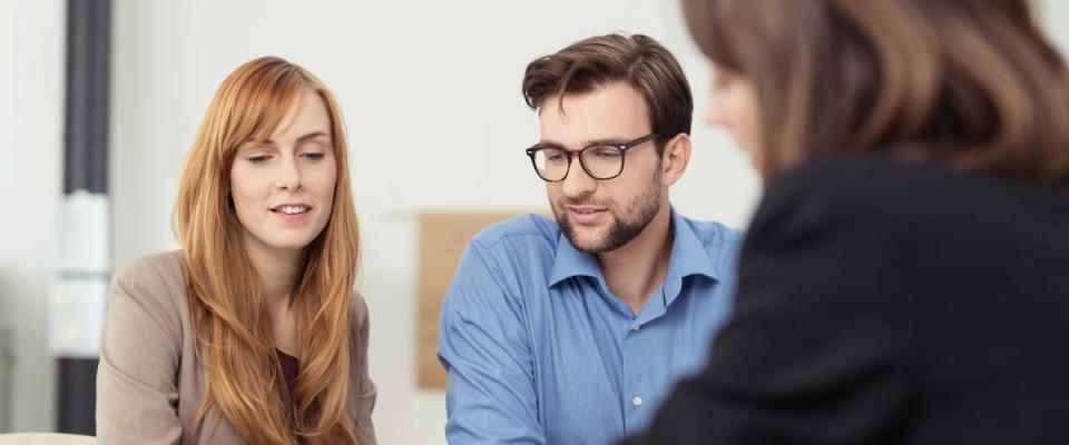 Broker making a presentation to a young couple showing them a document which they are viewing