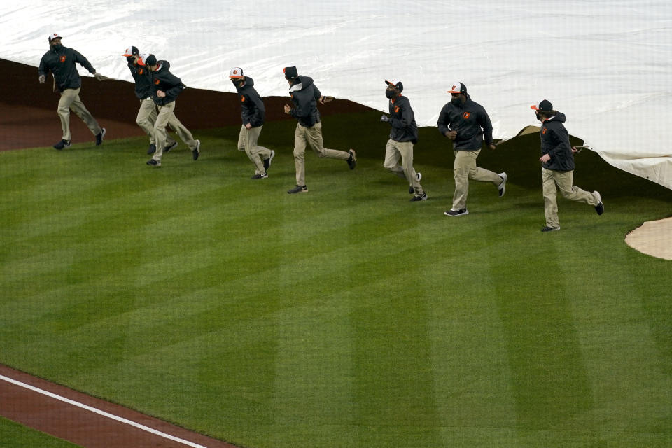 Grounds crew members place a tarp over the infield at Oriole Park at Camden Yards prior to a baseball game between the Baltimore Orioles and the Seattle Mariners, Monday, April 12, 2021, in Baltimore. (AP Photo/Julio Cortez)