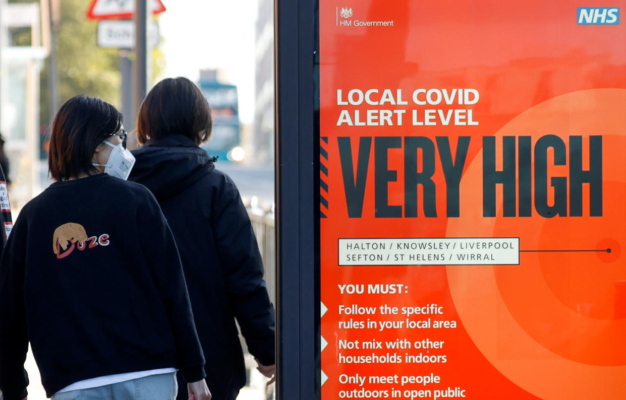 A person wearing a protective mask walks past a covid warning sign as the spread of the coronavirus disease (COVID-19) continues, in Liverpool, Britain October 15, 2020. REUTERS/Phil Noble