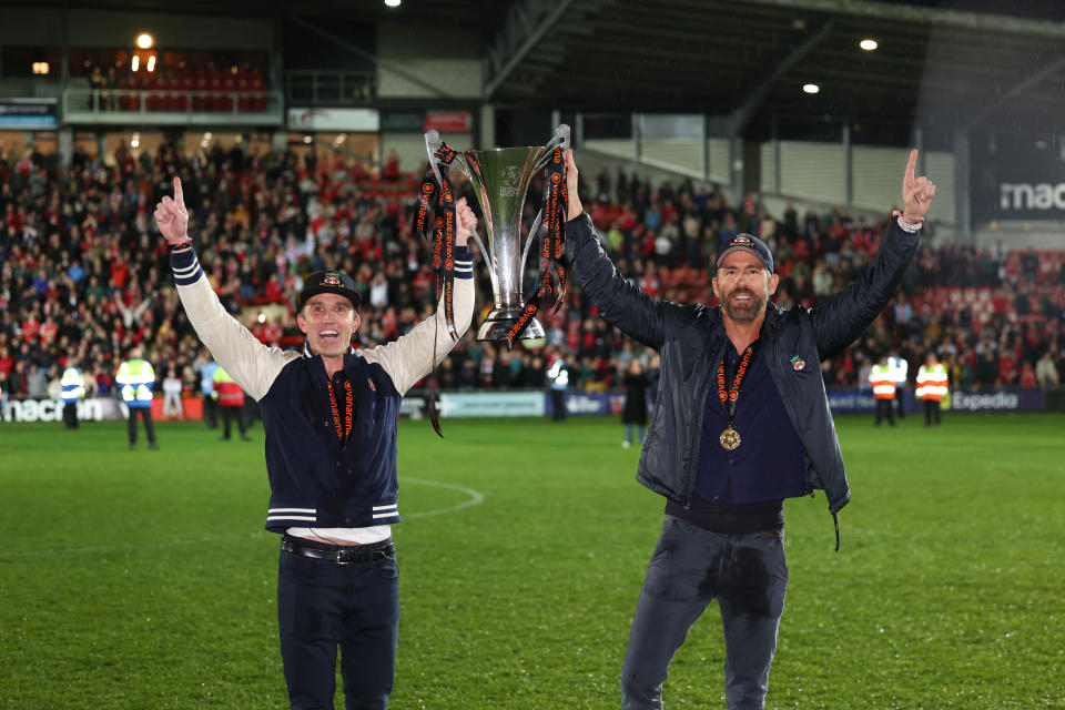 WREXHAM, WALES - APRIL 22: Wrexham owners Rob McElhenney and Ryan Reynolds hold the Vanarama National League Trophy as Wrexham celebrate promotion back to the English Football League during the Vanarama National League match between Wrexham and Boreham Wood at Racecourse Ground on April 22, 2023 in Wrexham, Wales. (Photo by Matthew Ashton - AMA/Getty Images)