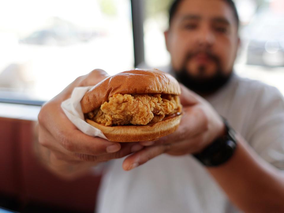 A man holds up a Popeyes chicken sandwich.