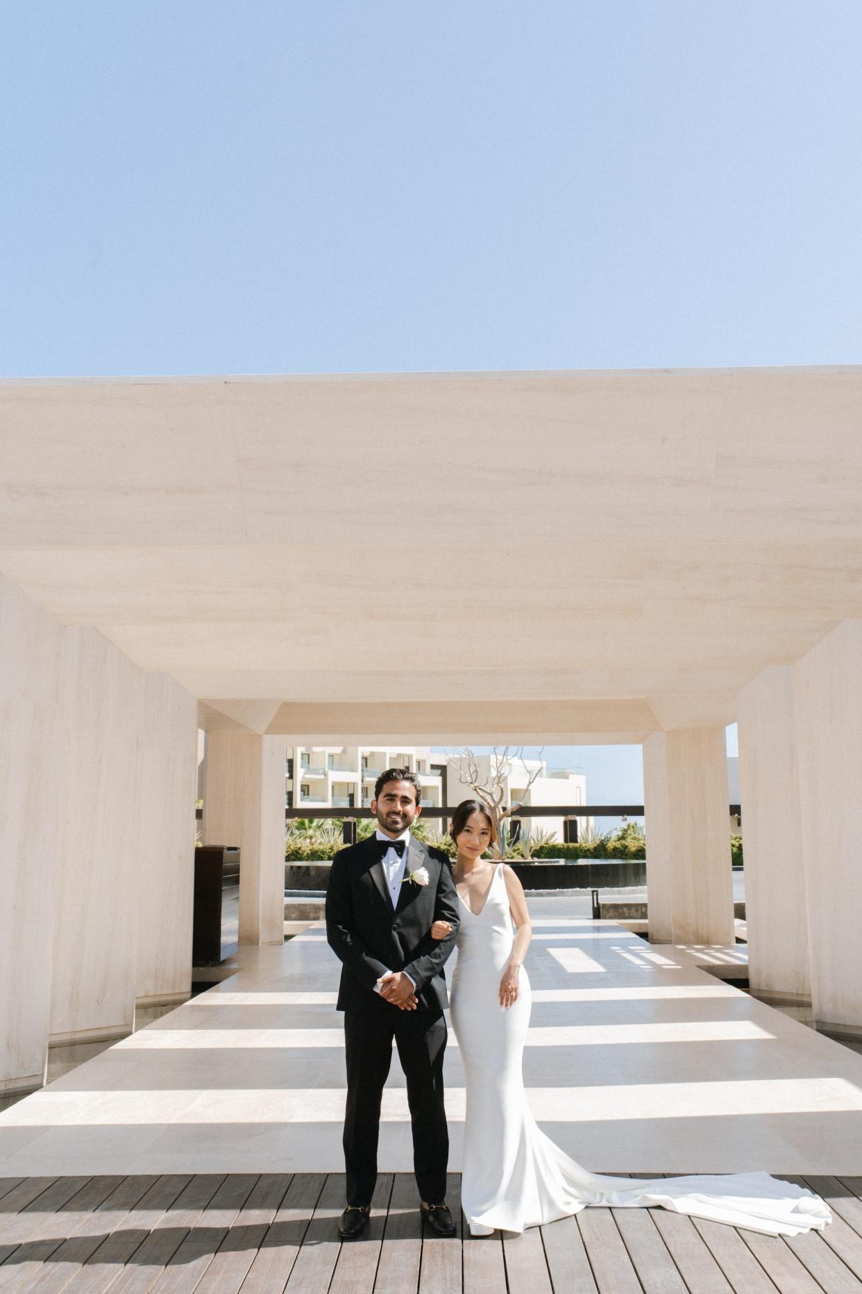 A couple poses in their wedding attire in front of stone arches.