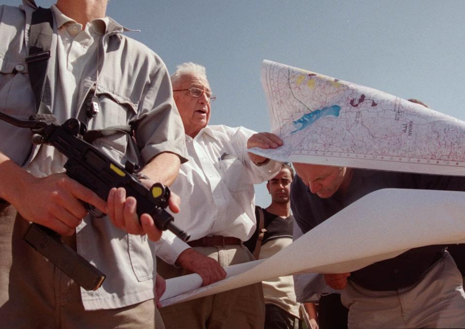 FILE - In this Thursday, Oct. 14, 1999 file photo, Ariel Sharon, center, leader of the opposition Likud party, unfurls maps of Israeli settlements in the West Bank with right-wing Knesset member Hanan Porat, right, during a tour of the West Bank settlement of Har Harasha northwest of Ramallah. Sharon, the hard-charging Israeli general and prime minister who was admired and hated for his battlefield exploits and ambitions to reshape the Middle East, died Saturday, Jan. 11, 2014. The 85-year-old Sharon had been in a coma since a debilitating stroke eight years ago. (AP Photo/Jacqueline Larma, File)