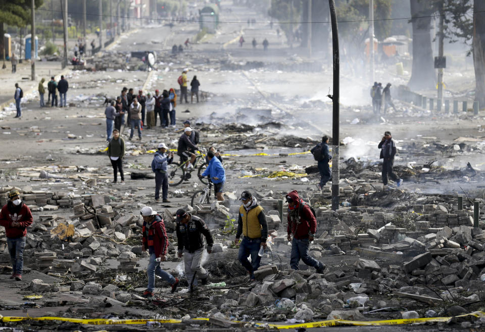 Pedestrians walk among the debris of barricades set by anti-government protesters in Quito, Ecuador, Sunday, Oct. 13, 2019. President Lenin Moreno ordered the army onto the streets of Ecuador's capital Saturday after a week and a half of protests over fuel prices devolved into violent incidents. (AP Photo/Fernando Vergara)