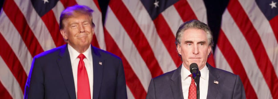 Doug Burgum speaks during a Nevada Republican caucus night watch party in Las Vegas as Donald Trump listens