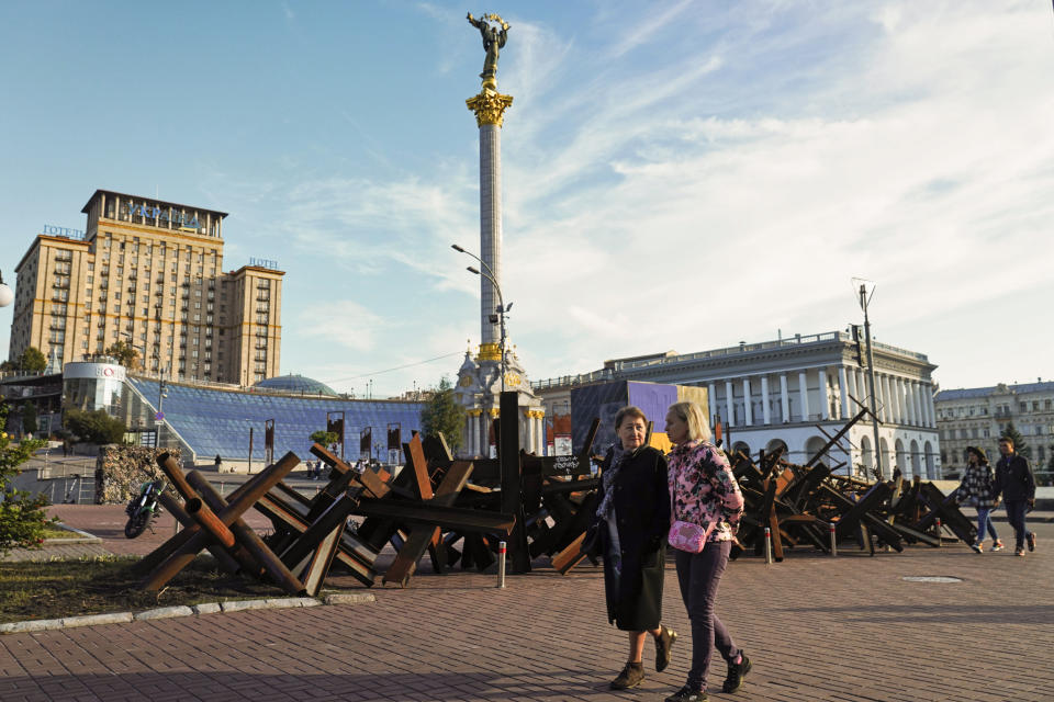 Image: Two women walk by rusted hedgehogs once put in the streets to block tanks and the Independence Monument in Kyiv, on  Sept. 11, 2022. (Jon Gambrell / AP)