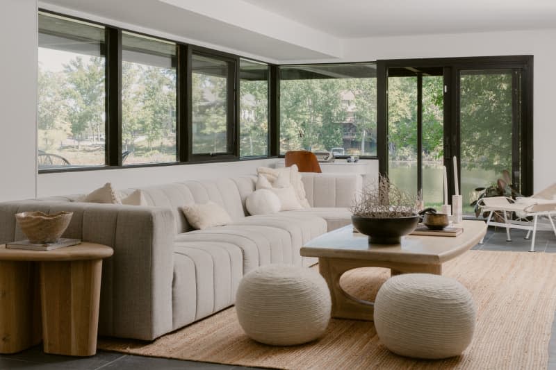 Large beige tufted sofa in a living room, with natural fiber rug, natural fiber poufs, over-sized wooden coffee table and side table.