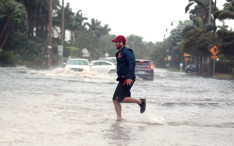 A man jogs through a flooded road in Palm Beach, Fla.