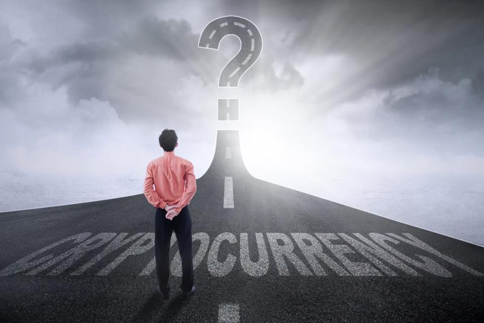 Person standing on a highway marked Cryptocurrency, looking up at the road forming a giant question mark in the sky.