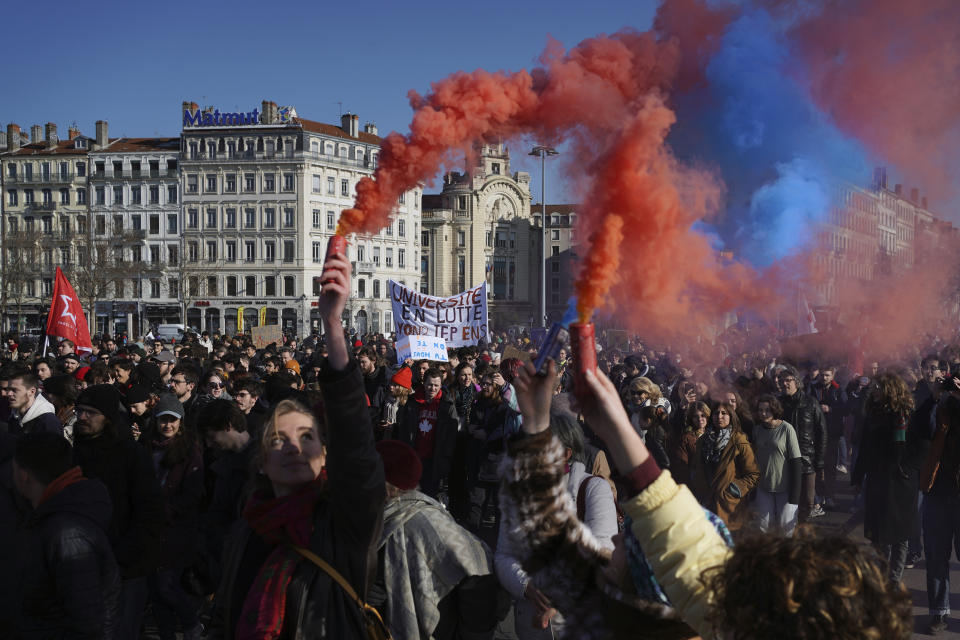 Demonstrators, holding colored flares, march against pension reforms in Lyon, central France, Tuesday, Feb. 7, 2023. Public transportation, schools and electricity, oil and gas supplies were disrupted on Tuesday in France as demonstrators are taking to the streets for a third round of nationwide strikes and protests against the government's pension reform plans. (AP Photo/Laurent Cipriani)