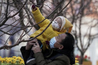A man holds up a child, both wearing face masks to help curb the spread of the coronavirus, to reach out a tree branches at the Wangfujing shopping district in Beijing, Monday, Jan. 18, 2021. A Chinese province grappling with a spike in coronavirus cases is reinstating tight restrictions on weddings, funerals and other family gatherings, threatening violators with criminal charges. (AP Photo/Andy Wong)