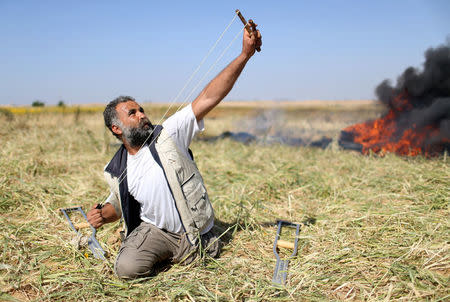 A Palestinian hurls stones at Israeli troops during clashes at the Gaza-Israel border at a protest demanding the right to return to their homeland, in the southern Gaza Strip March 31, 2018. REUTERS/Ibraheem Abu Mustafa