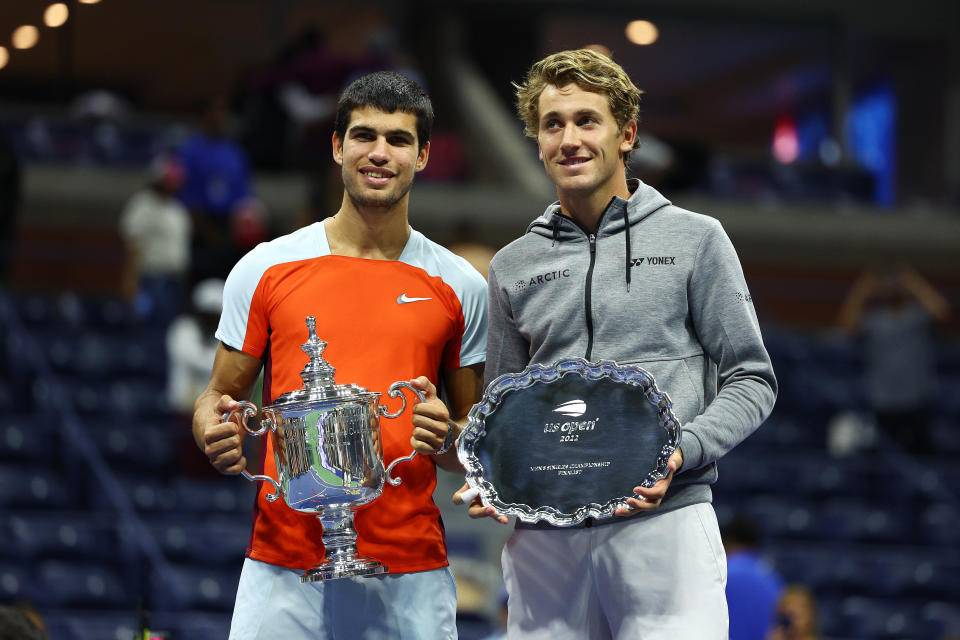 Casper Ruud (pictured right) holds the runner-up trophy alongside Carlos Alcaraz (pictured left) who celebrates with the championship trophy at the US Open.