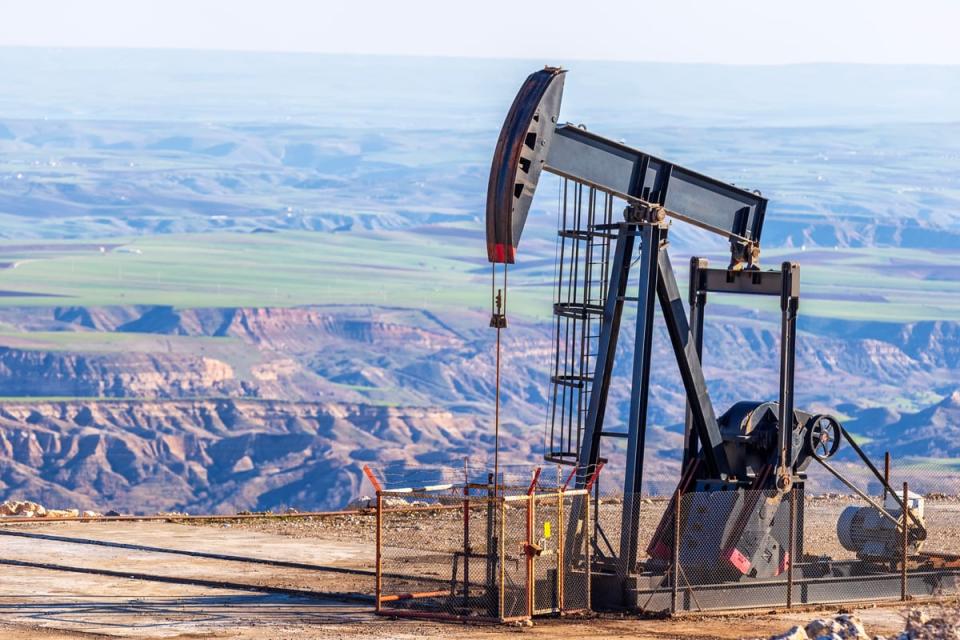 A pumpjack on a hill with a valley in the background. 