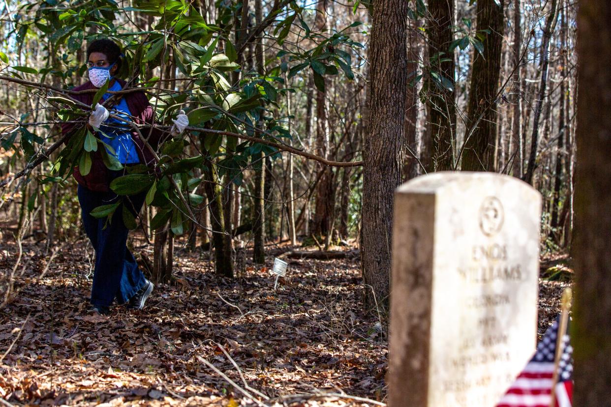 Amber Prentiss, a librarian, carries brush to a pile while volunteering as a gravestone is seen in the foreground at the Brooklyn Cemetery for the annual MLK Day of Service in Athens, Ga., on Martin Luther King Jr. Day, Monday, Jan. 18, 2021. Hundreds of volunteers showed up for shifts at over 20 locations to celebrate and honor the late civil rights hero.
