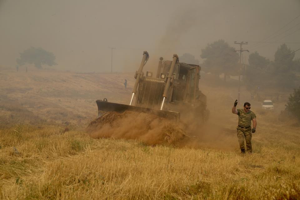 A military bulldozer opens fire break during a wildfire in Agios Stefanos, in northern Athens, Greece, Friday, Aug. 6, 2021. Thousands of people have fled wildfires burning out of control in Greece and Turkey, including a major blaze just north of the Greek capital of Athens that left one person dead. (AP Photo/Thanassis Stavrakis)