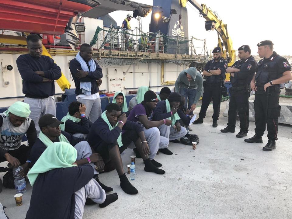 FILE -- In this file photo migrants sit on the quay after disembarking at Lampedusa harbor, Italy, on June 29, 2019. Small boats filled with more Tunisian migrants have reached a tiny Italian island, which had no room to quarantine them Saturday, Aug. 1, 2020, amid the pandemic. Sicilian daily Giornale di Sicilia quoted Lampedusa Mayor Toto' Martello as saying the island can’t wait until the government sends a ferry as promised so they can be safely isolated for 14 days as part of anti-COVID-19 measures. (AP Photo/Annalisa Camilli)