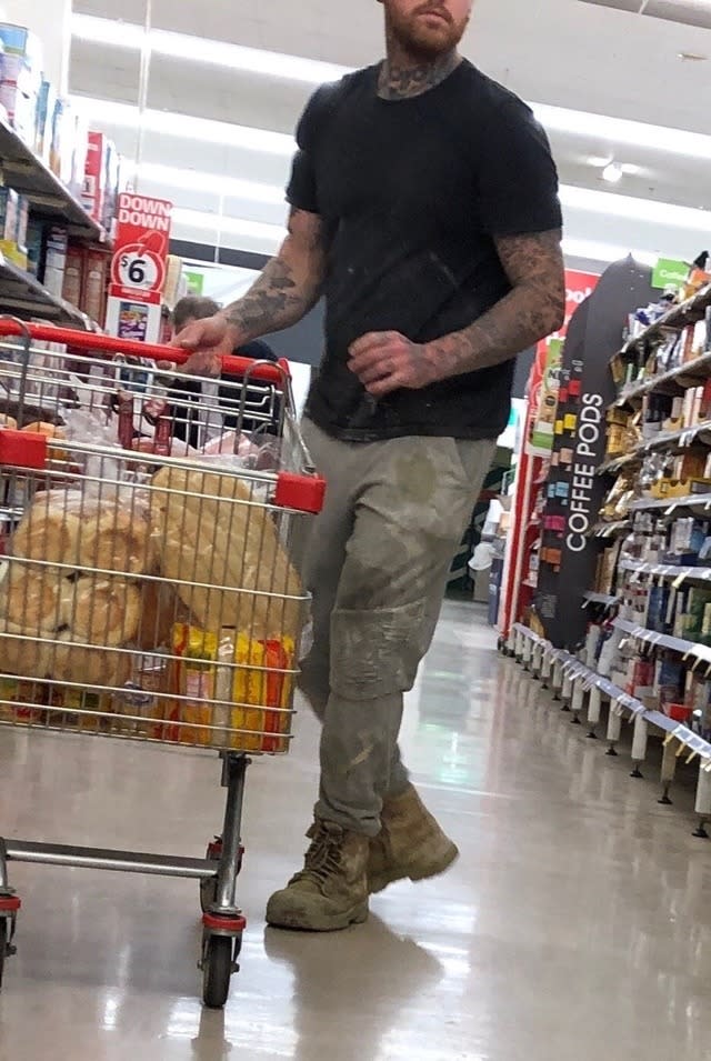 A tattooed man can be seen in the Coles aisle from the nose down. 