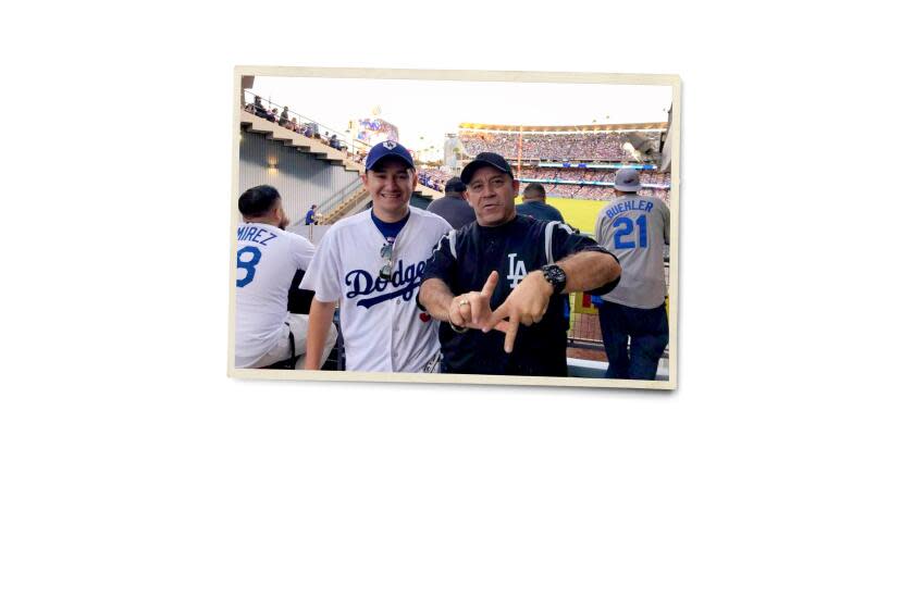 A photograph of a two men at a Dodgers game. David Porras, on right, is holding up his fingers in the sign of LA.