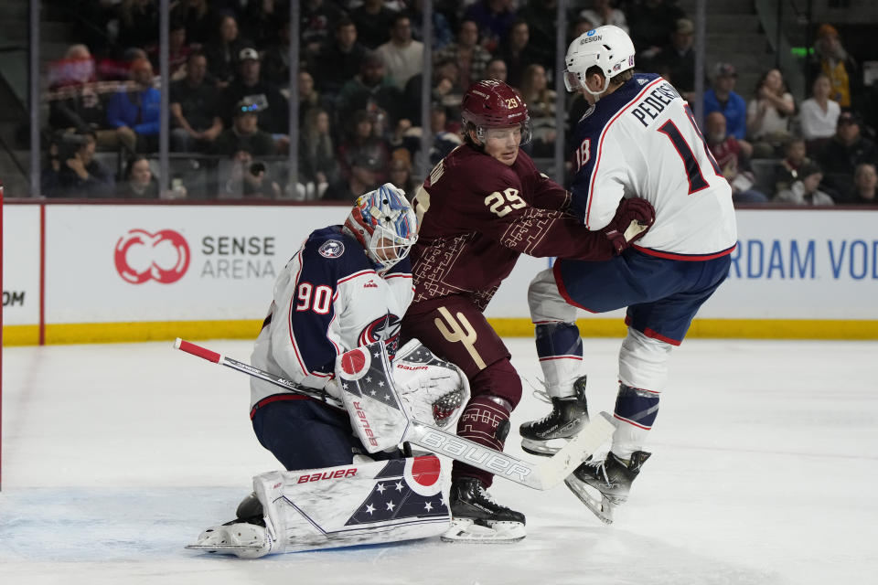 Columbus Blue Jackets goaltender Elvis Merzlikins makes a save in front of center Lane Pederson (18) and Arizona Coyotes center Barrett Hayton (29) during the first period during an NHL hockey game Sunday, Feb. 19, 2023, in Tempe, Ariz. (AP Photo/Rick Scuteri)