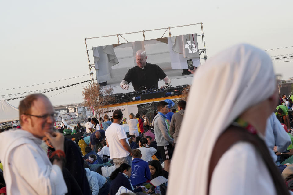 Roman Catholic priest Guilherme Peixoto, on video screen, plays techno music to help pilgrims wake up at Parque Tejo in Lisbon on Sunday, Aug. 6, 2023, where Pope Francis will preside over a mass celebrating the 37th World Youth Day later in the day. Before an estimated 1.5 million faithful, Peixoto swayed to the dance beat he mixed with clips of papal speeches. (AP Photo/Ana Brigida)