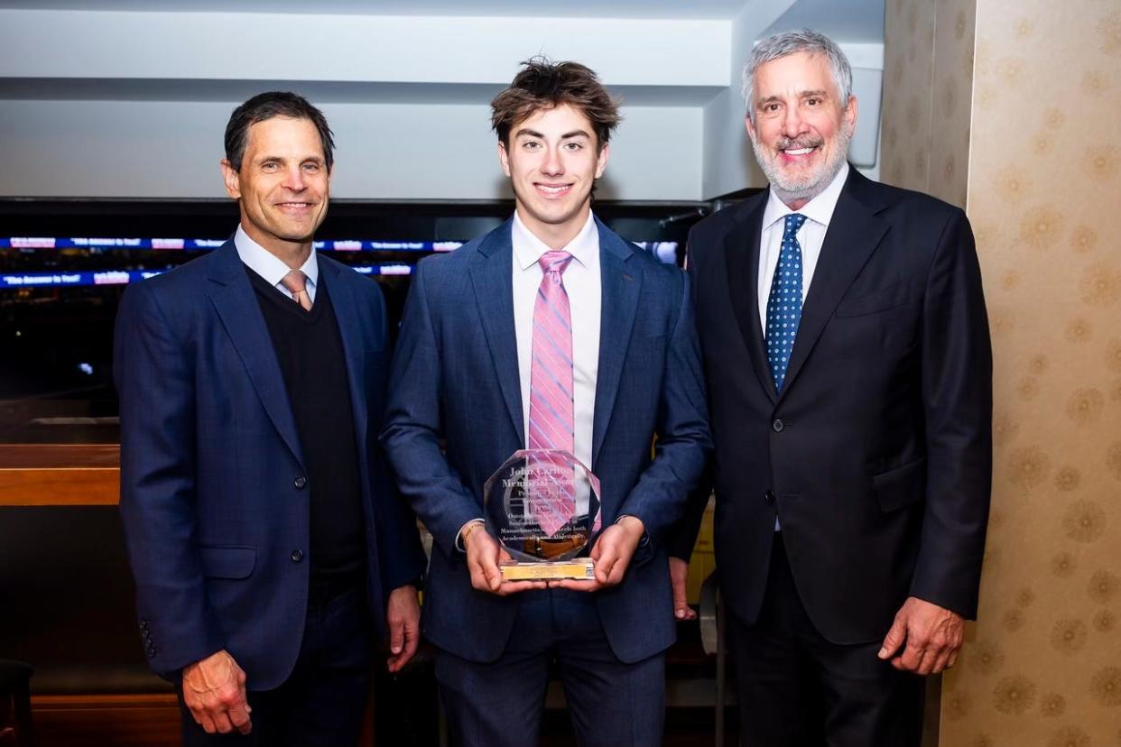 Austin Borgaard, center, posing with the John Carlton Memorial Trophy and Bruins executives Don Sweeney, left, and Cam Neely.