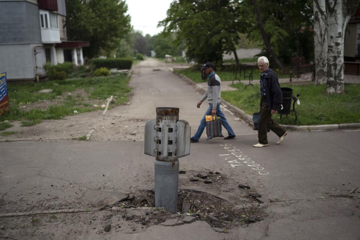 FILE - People walk past part of a rocket that sits wedged in the ground in Lysychansk, Luhansk region, Ukraine, on May 13, 2022. 