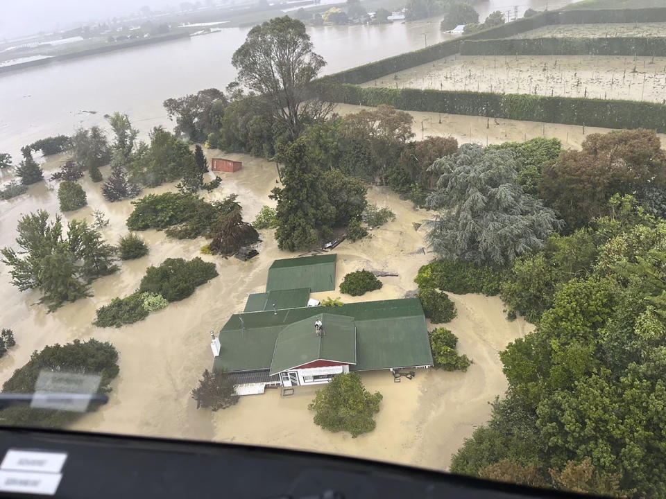 In this image released by the New Zealand Defense Force on Wednesday, Feb. 15, 2023, people stand on a rooftop of a home waiting to be winched to safety by helicopter in the Esk Valley, near Napier, New Zealand. The New Zealand government declared a national state of emergency Tuesday after Cyclone Gabrielle battered the country's north in what officials described as the nation's most severe weather event in years. (New Zealand Defense Force via AP)