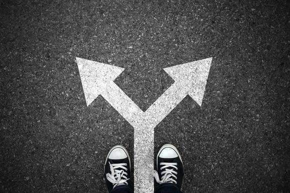 An arrow splitting into two drawn on the pavement in the middle of a pair of sneakers.