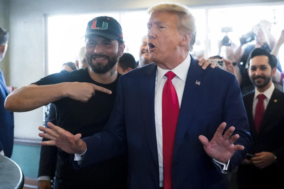 ADDS NAME OF PERSON AT LEFT - UFC fighter Jorge Masvidal gestures towards former President Donald Trump as he visits Versailles restaurant on Tuesday, June 13, 2023, in Miami. Trump appeared in federal court Tuesday on dozens of felony charges accusing him of illegally hoarding classified documents and thwarting the Justice Department's efforts to get the records back. (AP Photo/Alex Brandon)