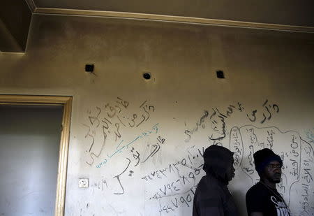 Sudanese immigrants are seen in front of a wall covered in graffiti names inside a deserted textile factory in the western Greek town of Patras April 28, 2015. REUTERS/Yannis Behrakis