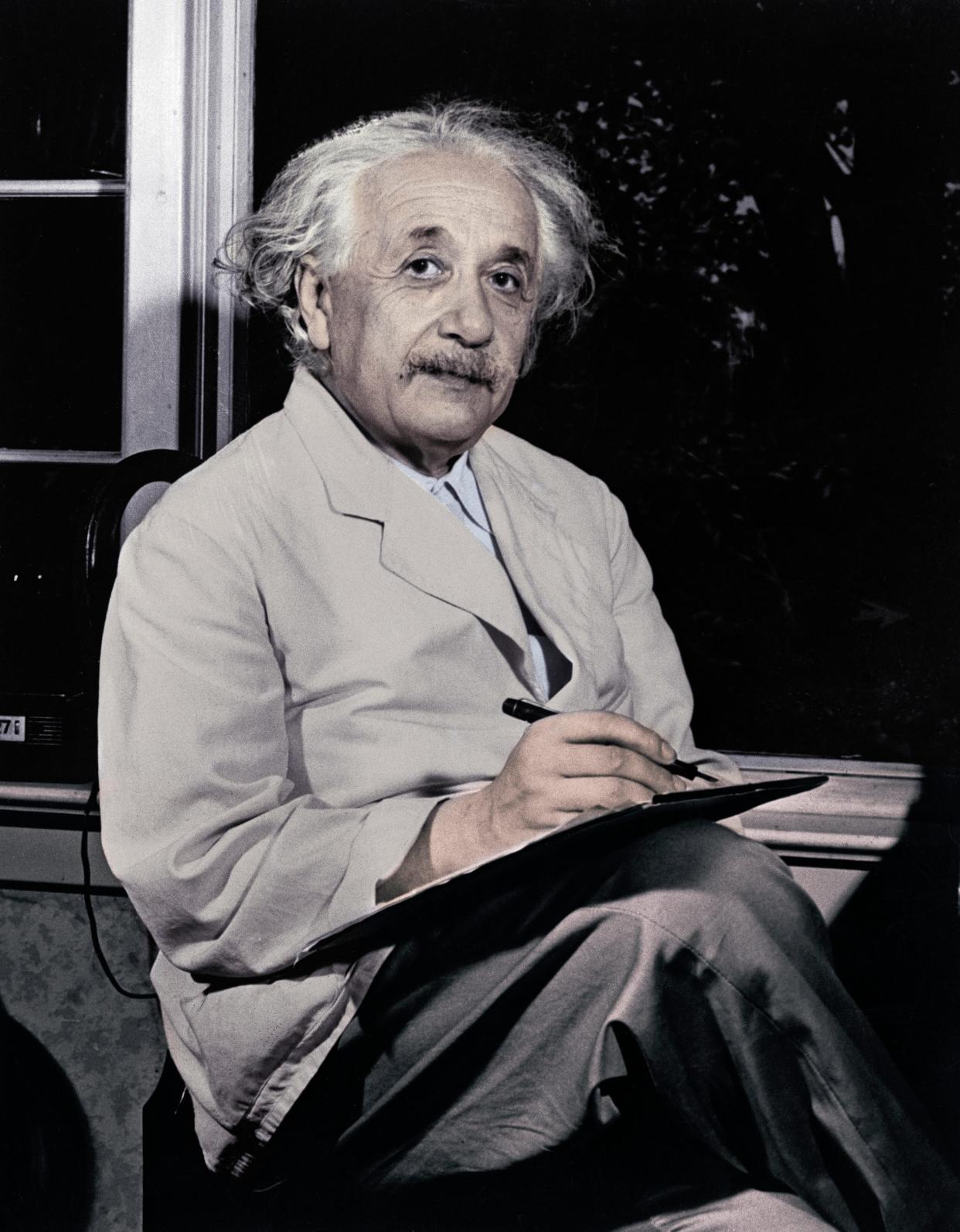 Dr. Albert Einstein is shown seated inside by the window, writing.