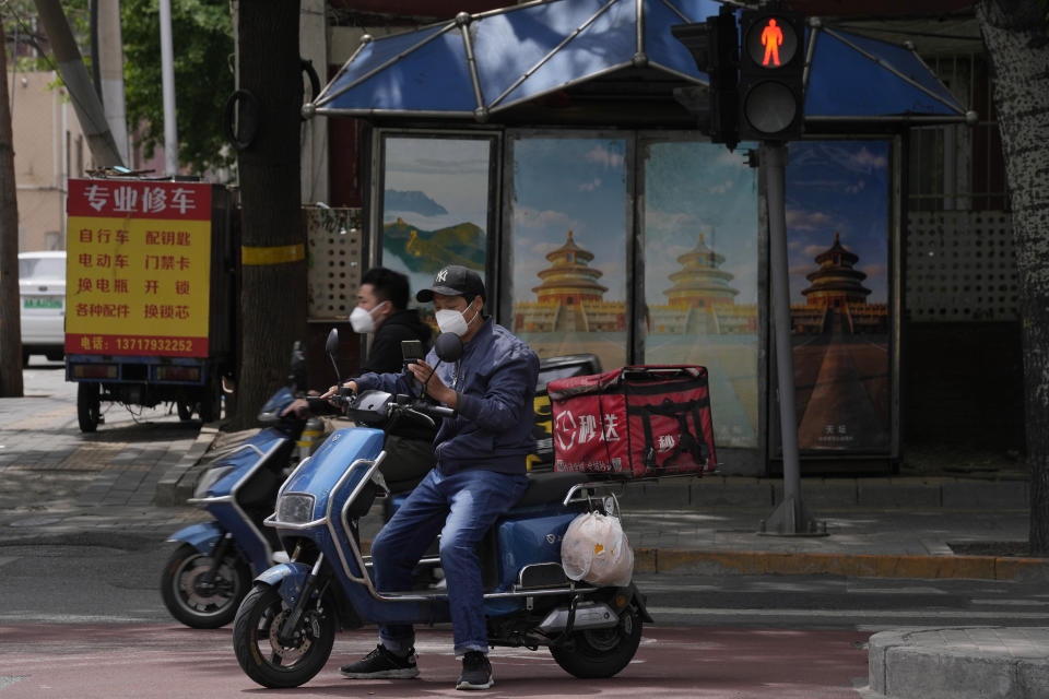 A delivery man checks his phone, as another moves past a shuttered news stand on a quiet street on Wednesday, May 11, 2022, in Beijing. (AP Photo/Ng Han Guan)