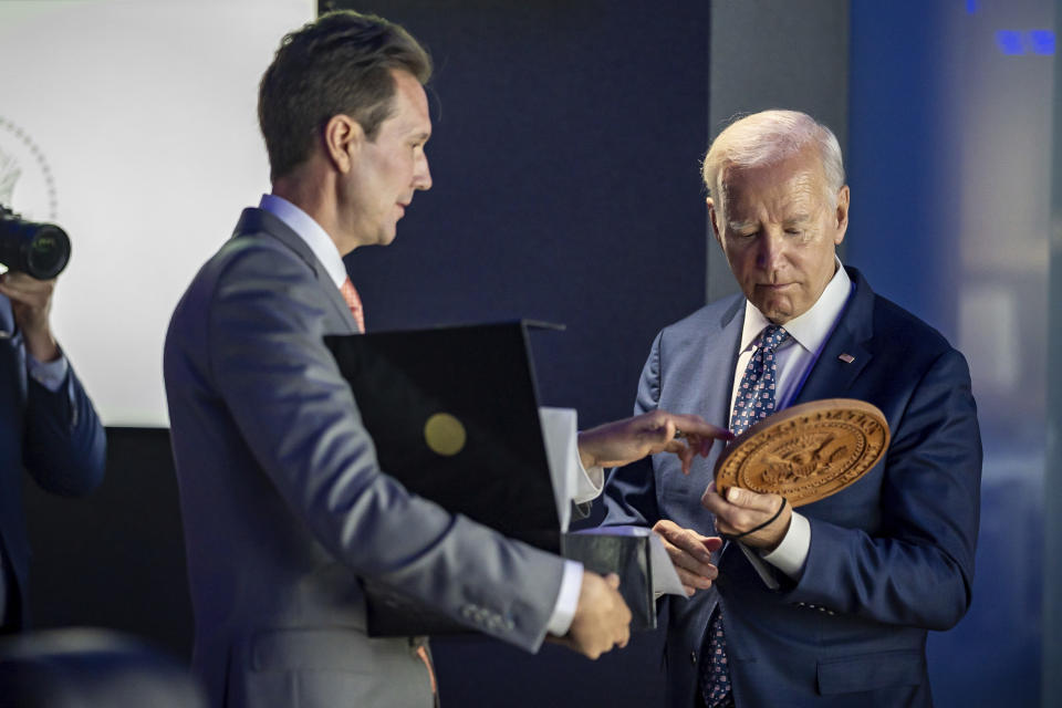 In this image provided by the White House, President Joe Biden looks at a wooden presidential seal presented to him by Situation Room director Marc Gustafson, left, as tours the "watch floor" in renovated White House Situation Room complex , Sept. 5, 2023, in the West Wing of the White House in Washington. The 5,500-square-foot, highly secure complex of conference rooms and offices in the West Wing has undergone a gut renovation that took a year to complete. (Carlos Fyfe/The White House via AP)