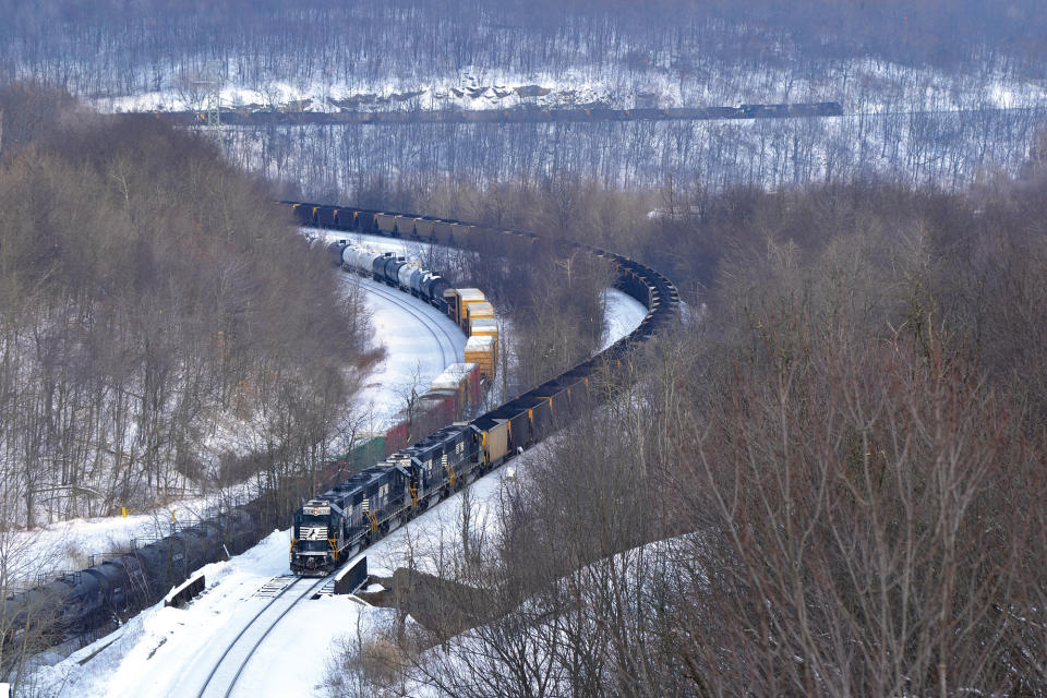 Norfolk Southern trains snake through a snow-covered mountain pass.