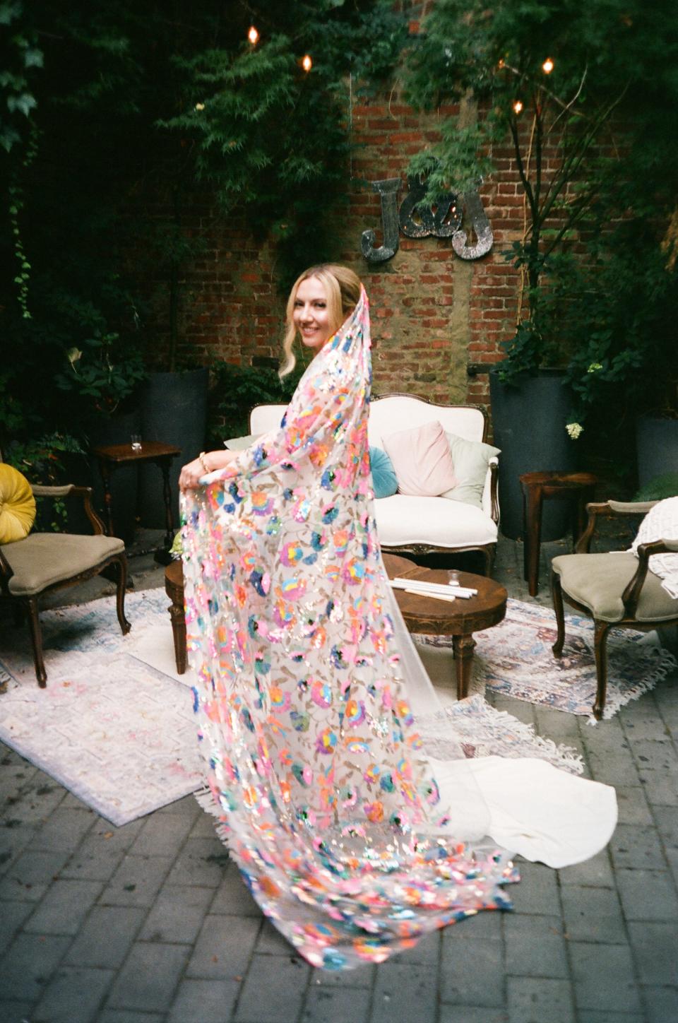 A bride pulls her floor-length rainbow veil around her.