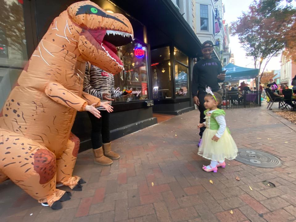 One-year-old Kiln Harp is dressed as Tiana from "The Princess and The Frog" as she meets a friendly dinosaur Friday during the Halloween Block Party in downtown Hagerstown.