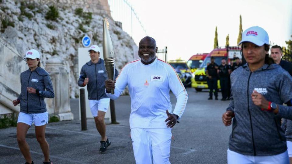 Former French footballer Basile Boli holds the Olympic torch as part of the Olympic and Paralympic torch relay at the Notre Dame de la Garde Basilica