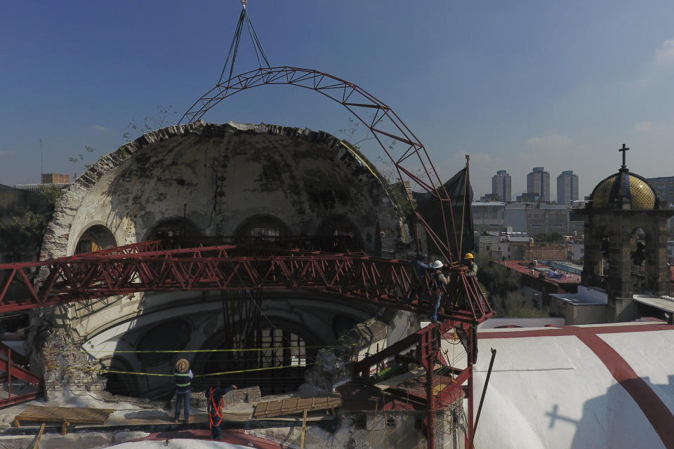 Workers guide into place a steel arch lowered by a crane, as part of a frame that will support a temporary metal roof overtop the damaged cupola, in the early stages of reconstruction work at Nuestra Senora de Los Angeles, or Our Lady of Angels church, three years after an earthquake collapsed nearly half of its 18th-century dome in Mexico City, Wednesday, Sept. 23, 2020. It is so dangerous to stand beneath the remains of the dome that the tons of steel structures are made off-site and then gingerly lowered into the crater at the center where the dome once stood. (AP Photo/Rebecca Blackwell)