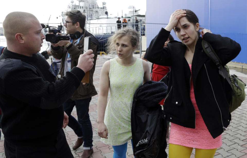 A Russian security officer records members of the punk group Pussy Riot Nadezhda Tolokonnikova, right, and Maria Alekhina, center, after they were attacked by Cossack militia in Sochi, Russia, on Wednesday, Feb. 19, 2014. Cossack militia attacked the Pussy Riot punk group with horsewhips on Wednesday as the group tried to perform under a sign advertising the Sochi Olympics. (AP Photo/Morry Gash)