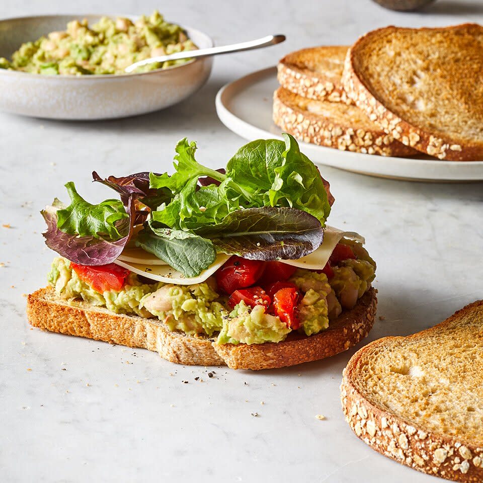 an open-face sandwich with avocado, beans, and veggies on a white granite counter