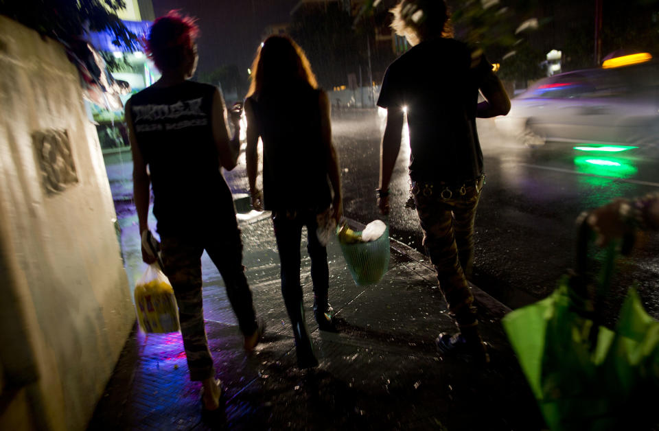 In this Monday, July 1, 2013 photo, a group of punks, including members of punk rock band Rebel Riot, walk with bags of food in a street, looking for homeless people during a weekly routine food distribution in Yangon, Myanmar. Punk rockers draw double-takes as they dart through traffic, but it's not the pink hair, leather jackets, or skull tattoos that make these 20-somethings rebels: It's their willingness to speak out against Buddhist monks instigating violence against Muslims while others in Myanmar are silent. (AP Photo/Gemunu Amarasinghe)