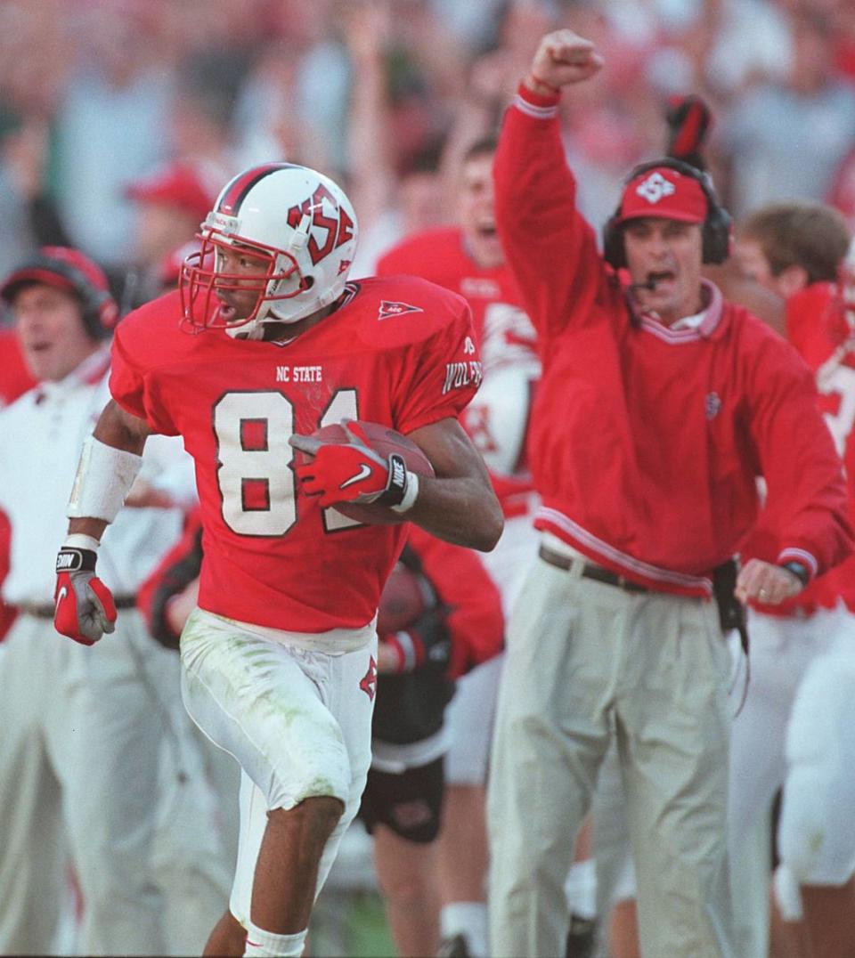 N.C. State’s head coach Mike O’Cain (background) cheers on wide receiver Torry Holt as he returns a punt for a touchdown in 1998 against North Carolina in Charlotte. UNC won the game, 37-34, in overtime.